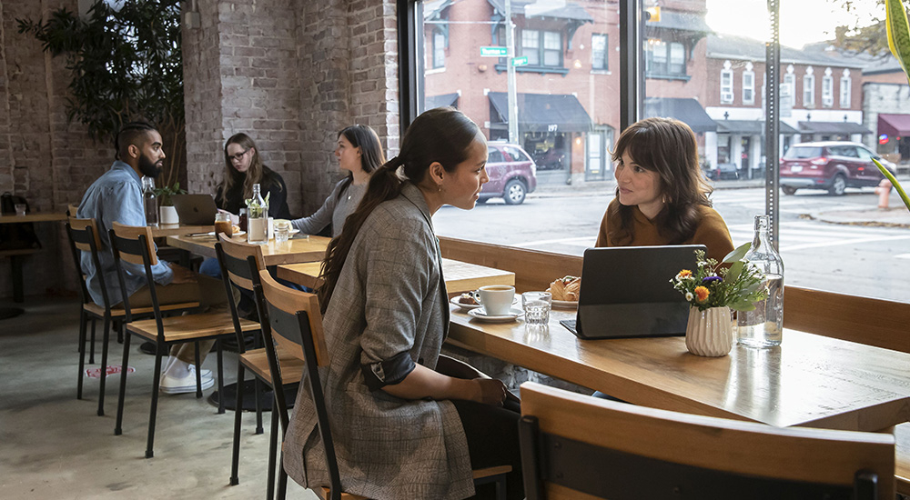 Two women at a coffee shop talking and looking at a tablet